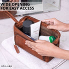 Toilettas van bruin leer (maraska), brede opening met handen zichtbaar, interieur en STILORD-logo zichtbaar