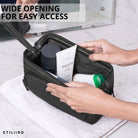 Leren toilettas zwart met brede opening, interieurzicht met handen en verzorgingsproducten op handdoek, STILORD embossing zichtbaar